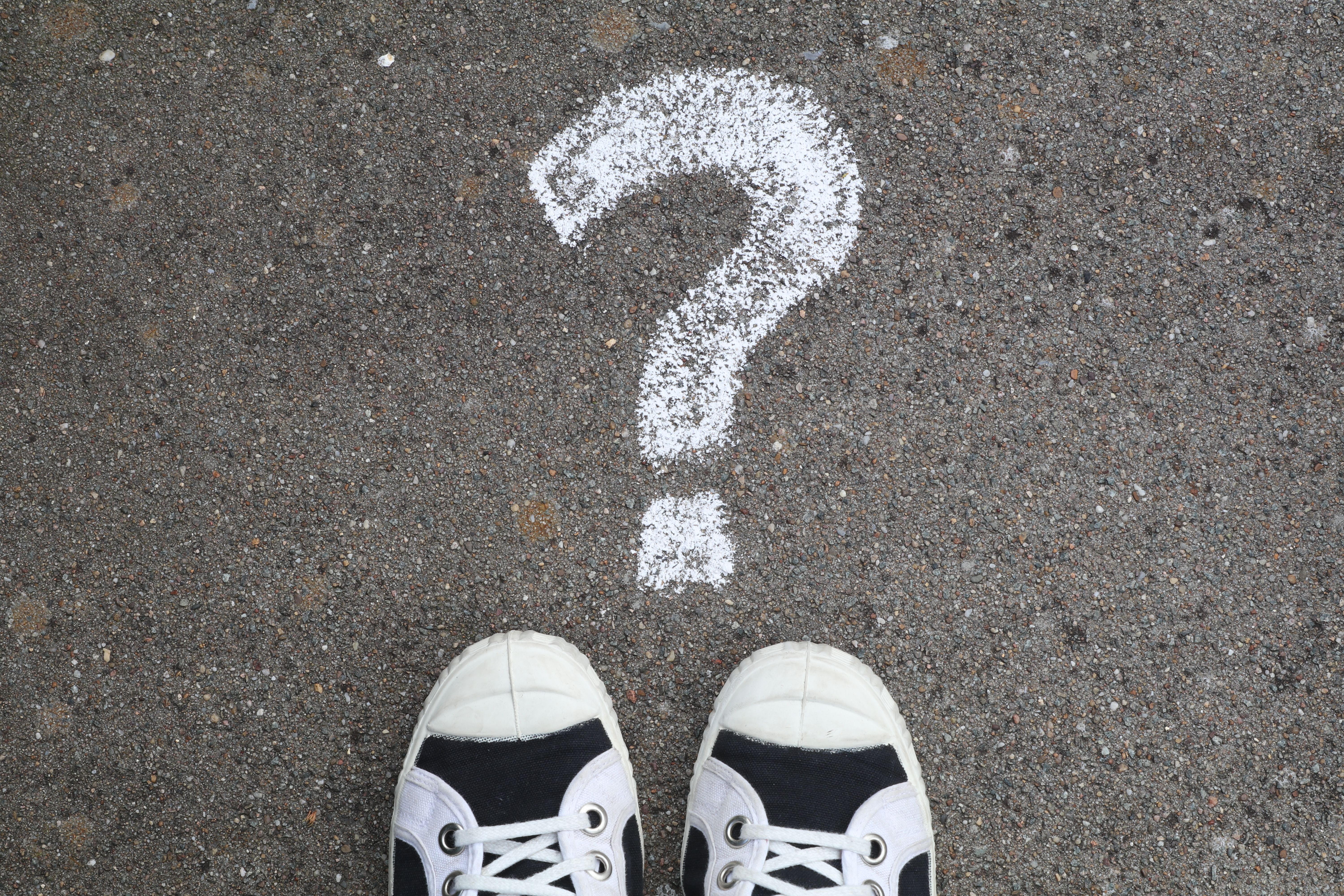 Sneakers on pavement with a chalk question mark, symbolizing curiosity or decisions.