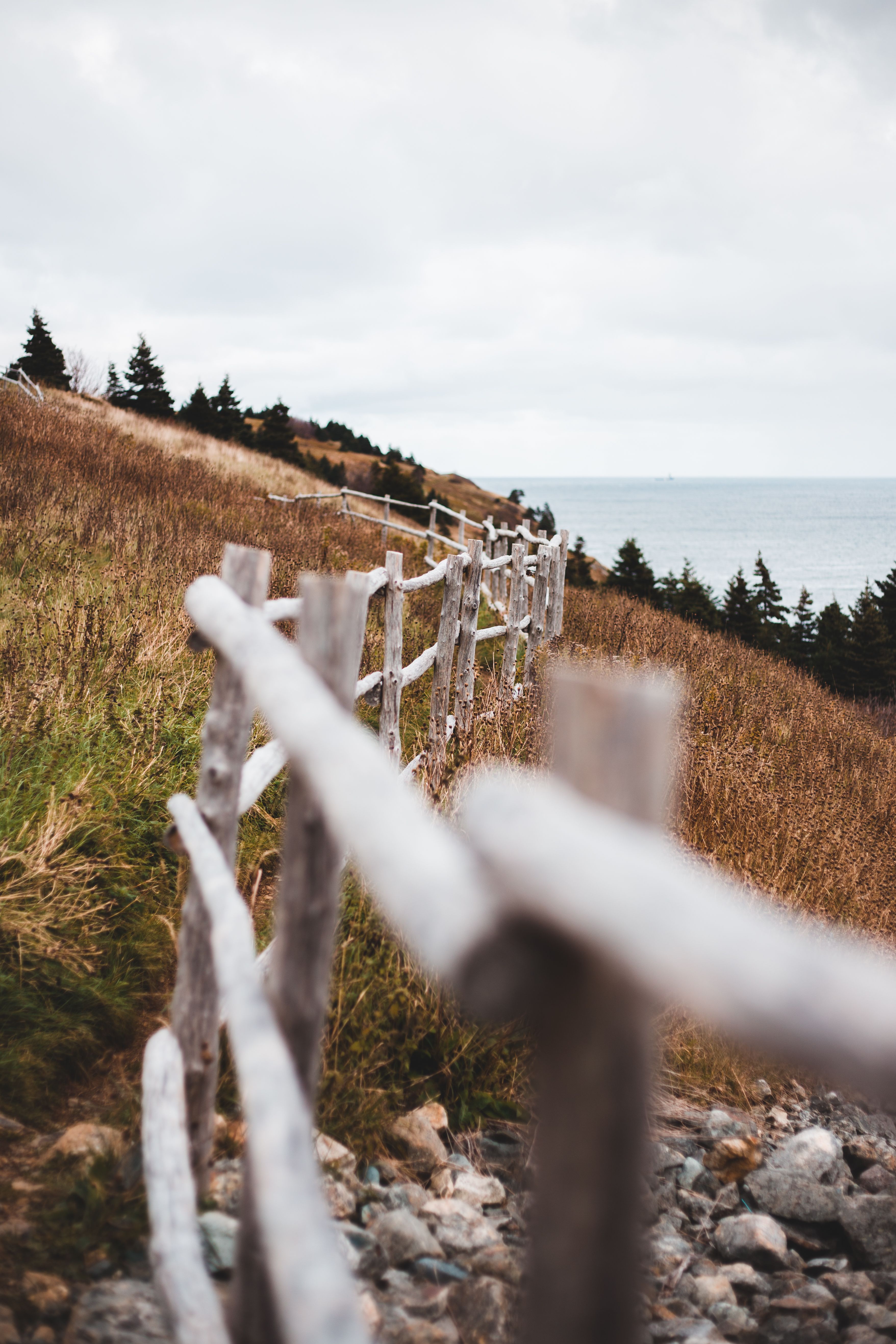 Long weathered wooden fence located on hill covered with dry grass against cloudy sky in countryside