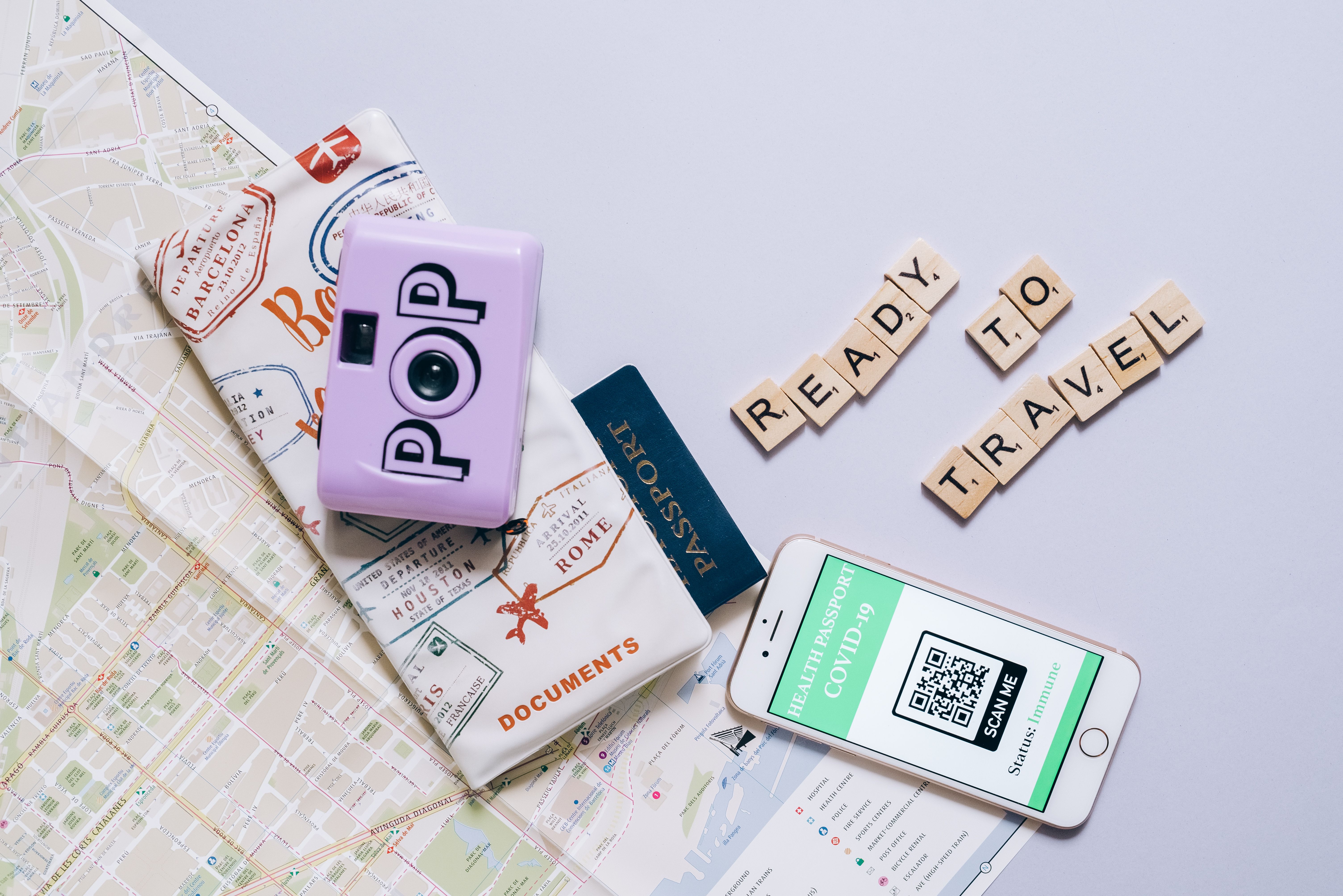 Travel essentials including a map, passport, camera, and smartphone with COVID-19 health passport for modern travel preparations.